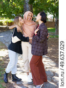 Group of young multiethnic girls best friends in casual clothes smiling and looking at camera while cuddling in park on sunny day. Delighted young diverse women embracing and smiling in park. Стоковое фото, агентство Ingram Publishing / Фотобанк Лори