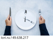 Intermitted farsting diet concept - empty plate and hands with fork and knife. Intermitted farsting diet concept. Стоковое фото, агентство Ingram Publishing / Фотобанк Лори