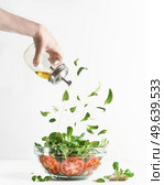 Woman hand pouring olive oil over green salad in glass bowl with tomatoes and flying lettuce leaves at white background. Healthy lifestyle. Salad making.Food levitation. Front view. Стоковое фото, агентство Ingram Publishing / Фотобанк Лори