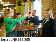 Multiracial man and women smiling and clinking glasses of alcohol beverages over table while proposing toast during meeting in bar. Diverse friends clinking glasses over table in beautiful pub. Стоковое фото, агентство Ingram Publishing / Фотобанк Лори
