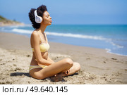 African American woman sitting on the beach doing mindfulness listening to a meditation with wireless headphones.. Black woman sitting on the beach doing mindfulness listening to a meditation with headphones. Стоковое фото, агентство Ingram Publishing / Фотобанк Лори