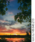 Gorgeous summer sunset as seen from the garden among the green trees. Sundown view over the city horizon reflected on the calm Delia lake water in Ungheni city, Moldova. Стоковое фото, агентство Ingram Publishing / Фотобанк Лори