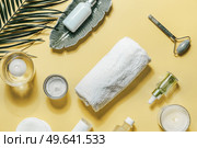 Beauty products for skin care on yellow background with palm leaf.  Facial cosmetics with towel, jade massage roller, candles, pipette bottles with serum and essential oil. Top view. Стоковое фото, агентство Ingram Publishing / Фотобанк Лори