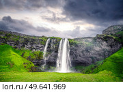 The beautiful Seljalandsfoss waterfall in Iceland surrounded by lava cliffs and green fields in a cloudy sunset. Стоковое фото, агентство Ingram Publishing / Фотобанк Лори