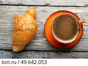 fresh boiled coffee served in beautiful orange cup with croissant around old style wooden background . close up. flat lay . Стоковое фото, агентство Ingram Publishing / Фотобанк Лори