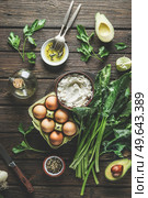 Preparing spinach ricotta stuffing with herbs, eggs and spices at dark wooden kitchen table. Cooking at home with fresh healthy ingredients. Top view. Стоковое фото, агентство Ingram Publishing / Фотобанк Лори