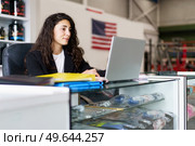 Glad sports psychologist smiling and browsing data on netbook while sitting at desk during work in gym in daytime. Positive woman preparing for psychology session in gym. Стоковое фото, агентство Ingram Publishing / Фотобанк Лори