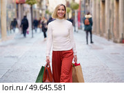 Positive female shopaholic carrying paper bags while strolling on pavement and looking at camera. Smiling woman carrying shopping bags on paved street. Стоковое фото, агентство Ingram Publishing / Фотобанк Лори