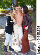 Positive young multiethnic female best friends in casual clothes smiling and looking at camera while cuddling in park on sunny day. Delighted young diverse ladies embracing and smiling in park. Стоковое фото, агентство Ingram Publishing / Фотобанк Лори