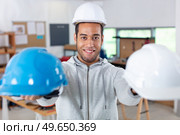 smiling man holding hardhats with his hands. Стоковое фото, агентство Ingram Publishing / Фотобанк Лори
