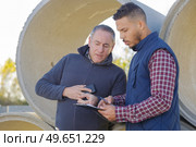 two coworkers discussing in cement pipes yard. Стоковое фото, агентство Ingram Publishing / Фотобанк Лори