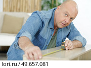 male carpenter uses measuring tape measure wood. Стоковое фото, агентство Ingram Publishing / Фотобанк Лори