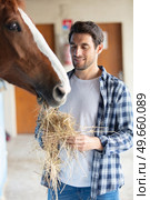 man in working clothes feeding horse with hay at stable. Стоковое фото, агентство Ingram Publishing / Фотобанк Лори