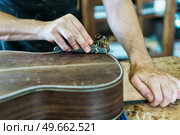 Crop craftsman using plane to shave traditional Spanish flamenco guitar on workbench in workshop. Unrecognizable male luthier crafting Spanish flamenco guitar. Стоковое фото, агентство Ingram Publishing / Фотобанк Лори