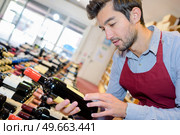 joyful male seller holding bottle wine in wine shop. Стоковое фото, агентство Ingram Publishing / Фотобанк Лори