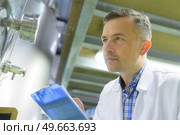 man wearing labcoat inspecting vat and holding clipboard. Стоковое фото, агентство Ingram Publishing / Фотобанк Лори