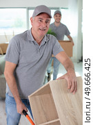 cheerful removals men moving a cupboard on a trolley. Стоковое фото, агентство Ingram Publishing / Фотобанк Лори