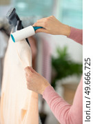 young woman cleaning her shirt with lint roller. Стоковое фото, агентство Ingram Publishing / Фотобанк Лори