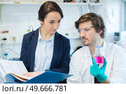 scientist holding beaker of pink liquid with woman holding folder. Стоковое фото, агентство Ingram Publishing / Фотобанк Лори