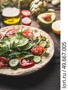 Healthy flatbread sandwich preparation with fresh tomato,cucumber and avocado on dark background with ingredients, close up. Стоковое фото, агентство Ingram Publishing / Фотобанк Лори