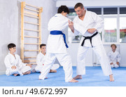 Male karate instructor training little child wearing kimono in dojo or jiu-jitsu in gym. Стоковое фото, фотограф Яков Филимонов / Фотобанк Лори