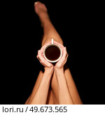 Top view of crop unrecognizable barefooted female sitting in black studio with cup of hot coffee. Crop anonymous woman with coffee cup in black studio. Стоковое фото, агентство Ingram Publishing / Фотобанк Лори