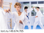 Diligent preteen attendee of karate classes fighting with his opponent in sports hall. Стоковое фото, фотограф Яков Филимонов / Фотобанк Лори