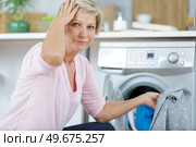 forgetful mature woman by washing machine holding jumper. Стоковое фото, агентство Ingram Publishing / Фотобанк Лори