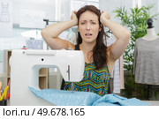 worried female tailor fixing stuck fabric at equipment. Стоковое фото, агентство Ingram Publishing / Фотобанк Лори
