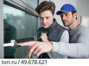 apprentice being advised how to apply caulk to window. Стоковое фото, агентство Ingram Publishing / Фотобанк Лори