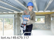 female builder with clipboard stood on stepladder. Стоковое фото, агентство Ingram Publishing / Фотобанк Лори