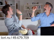 Father and son aiming popcorn into eachother's mouths. Стоковое фото, агентство Ingram Publishing / Фотобанк Лори