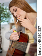 guitarist woman light a cigarette at home. Стоковое фото, агентство Ingram Publishing / Фотобанк Лори