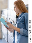 woman reading a book while doing her washing at laundromat. Стоковое фото, агентство Ingram Publishing / Фотобанк Лори