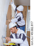two builders in hardhats and overalls with spatula repairing room. Стоковое фото, агентство Ingram Publishing / Фотобанк Лори