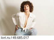 Portrait of self assured female model with curly hair in casual wear chilling and staring at camera seductively against white background. Determined woman resting and gazing at camera. Стоковое фото, агентство Ingram Publishing / Фотобанк Лори