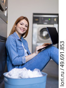 cheerful woman uses laptop computer waiting at the laundrette. Стоковое фото, агентство Ingram Publishing / Фотобанк Лори