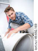 young male worker unrolling carpet on floor at home. Стоковое фото, агентство Ingram Publishing / Фотобанк Лори