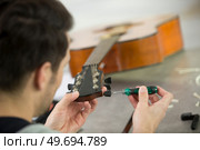 man repairing guitar tuning peg with a screwdriver. Стоковое фото, агентство Ingram Publishing / Фотобанк Лори