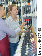 male seller showing bottle of wine to female customer. Стоковое фото, агентство Ingram Publishing / Фотобанк Лори