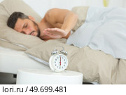 man with hand poised over alarmclock to silence it. Стоковое фото, агентство Ingram Publishing / Фотобанк Лори