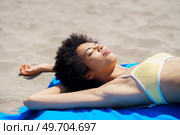 Happy young African American female tourist with curly hair in trendy bikini lying on sandy beach with closed eyes while sunbathing during summer holidays. Relaxed ethnic lady sunbathing on sandy shore on summer day. Стоковое фото, агентство Ingram Publishing / Фотобанк Лори