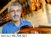 mature violin maker while testing the violins in his laboratory. Стоковое фото, агентство Ingram Publishing / Фотобанк Лори