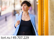 Portrait of confident female entrepreneur in formal clothes with handbag standing on blurred background street near yellow entrance and looking away. Stylish woman standing near yellow wall in daylight. Стоковое фото, агентство Ingram Publishing / Фотобанк Лори
