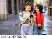 Two young Chinese females passing by guided by the GPS of their smartphone, through the streets of Granada, Spain. Concept of Asian people traveling in Europe.. Asian women travelers pointing away while walking on street. Стоковое фото, агентство Ingram Publishing / Фотобанк Лори
