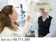 man reading text through phoropter during eye test. Стоковое фото, агентство Ingram Publishing / Фотобанк Лори