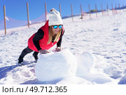 Full body of smiling young female in vest beanie wool cap polarized sunglasses looking away, while doing push ups on white snow rock against blurred wooden pillars fence in daylight. Happy woman doing exercise in warm clothes on snow rock. Стоковое фото, агентство Ingram Publishing / Фотобанк Лори