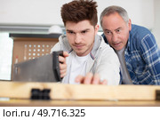 apprentice carpenter using a saw under supervision. Стоковое фото, агентство Ingram Publishing / Фотобанк Лори