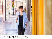 Confident cheerful female in trendy formal outfit looking at camera while standing on city street corridor against blurred background. Positive woman in formal wear standing on city street. Стоковое фото, агентство Ingram Publishing / Фотобанк Лори
