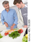 Man preparing vegetables, younger man looking on dubiously. Стоковое фото, агентство Ingram Publishing / Фотобанк Лори